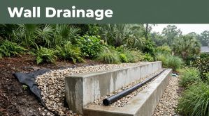 Concrete retaining wall with gravel, drain pipe, and lush plants after rain.
